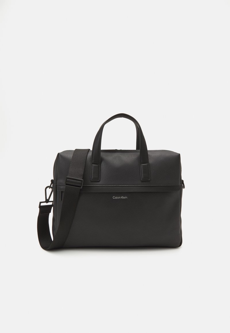 Borsa in pelle nera con texture a ciottoli, doppio manico e tracolla removibile. Presenta una chiusura con zip e il logo Calvin Klein sul fronte.