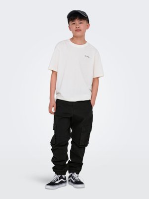 T-shirt blanc à manches courtes avec un petit motif, associé à un pantalon cargo noir avec plusieurs poches et des poignets élastiques, porté avec des baskets noires.