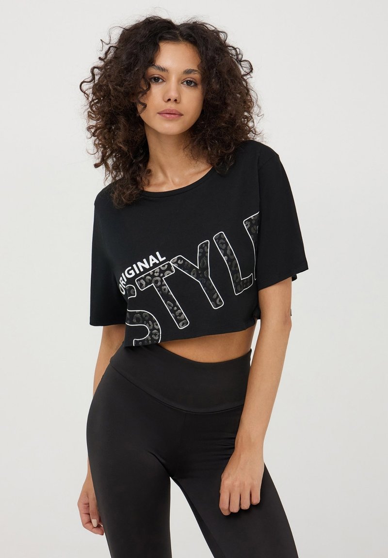 Maglietta nera corta con il testo "ORIGINAL STYLE" in un audace motivo leopardo. Abbinata a leggings neri a vita alta. Texture morbida.