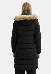 Schwarze gepolsterte Jacke mit einem mit Fell gefütterten Kapuzen, verfügt über horizontale Steppung, lange Ärmel und ein mittellanges Design.