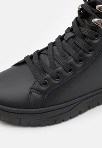 Zapatilla deportiva de cuero negro con un diseño de caña alta, cordones negros planos y acentos de hardware plateado en los ojales, además de una suela de goma texturizada.