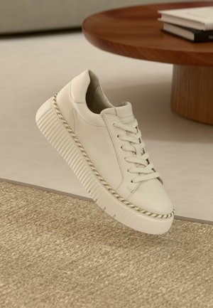 Hvit skinn-sneaker med tykk, teksturert såle og matchende lisser. Har en dekorativ sydd kant og et minimalistisk design.