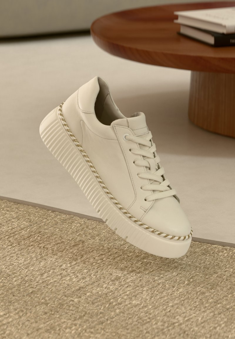 Fehér bőr sportcipő vastag, texturált talppal és hozzáillő fűzőkkel. Díszítő varrott szegéllyel és minimalista dizájnnal rendelkezik.