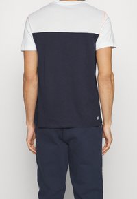 Kortärmad t-shirt med en marinblå kropp, vit mesh övre del och korallaccent på axeln, med en standard passform och mjuk textur.