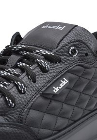 Czarne skórzane sneakersy z pikowaną fakturą, czarno-białymi sznurówkami oraz wypukłym logo na języku. Gumowa podeszwa i minimalistyczne akcenty z metalowymi elementami.