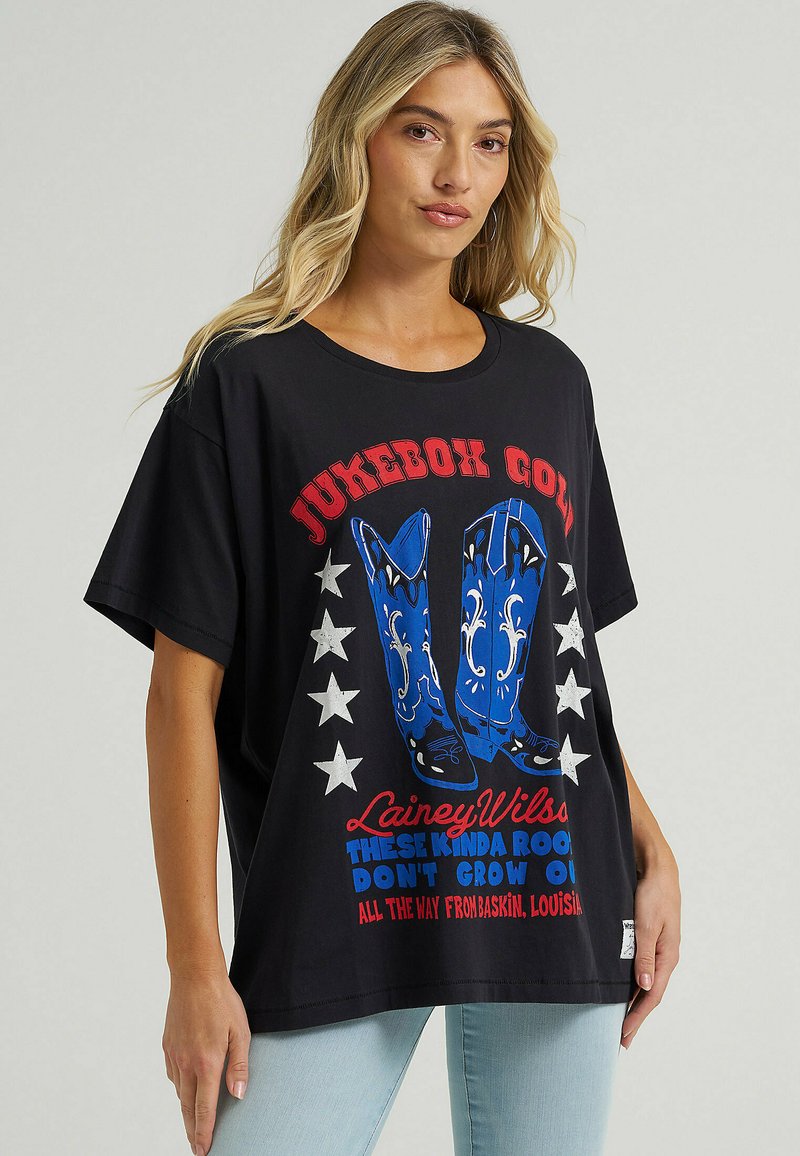 Camiseta negra de gran tamaño con gráficos de botas de vaquero azules, texto en rojo y blanco, estrellas plateadas y mangas cortas para un ajuste relajado.