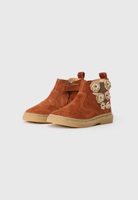 Stivaletti alla caviglia per bambini in suede marrone con suole in gomma e decorazioni floreali sui lati esterni, dotati di linguette e cinghie laterali.