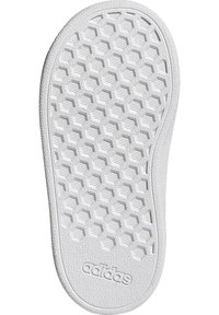 Semelle de chaussure en caoutchouc blanc avec un motif hexagonal pour l'adhérence, finition texturée et logo en relief sur le bord inférieur.
