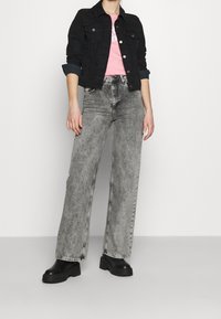 Černá denimová bunda přes růžové tričko, spárovaná se světle šedými širokými kalhotami a černými platformovými botami. Jednoduchý design s minimálními akcenty.