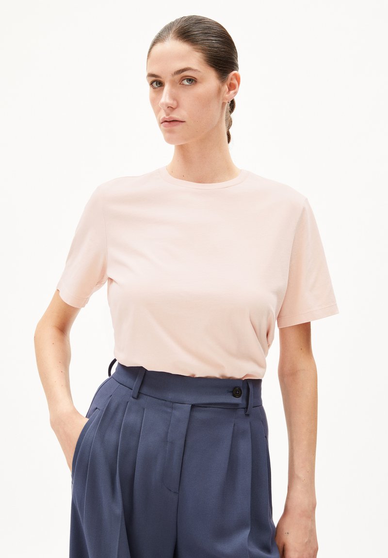 Lichtroze t-shirt met korte mouwen gemaakt van zachte stof, gedragen met hoge, marineblauwe broek met knoopdetails en plooien.