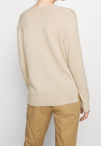 Beige stickad tröja med en avslappnad passform, långa ärmar och ribbat nederkant. Har rund halsringning och en mjuk textur.