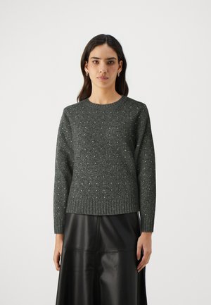 Maglione lavorato a maglia grigio scuro con collo rotondo, orlo a coste e macchie testurizzate. Il modello lo indossa con una gonna in pelle nera.