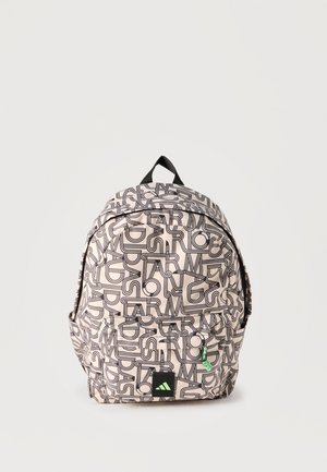 Mochila beige con un patrón de letras negras superpuestas en toda la superficie, bolsillo frontal con cremallera, asa negra y pequeño tirador de cremallera verde.