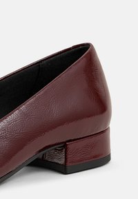 Chaussure plate en cuir verni bordeaux avec une finition texturée, un bout arrondi et un petit talon bloc, dotée d'une doublure intérieure noire.