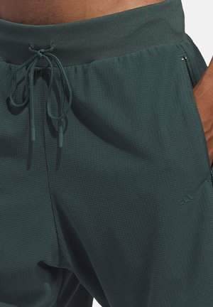 Donkergroene atletische joggers gemaakt van gestructureerde stof, voorzien van een trekkoorden tailleband en zijritszakken. Subtiele branding op het been.