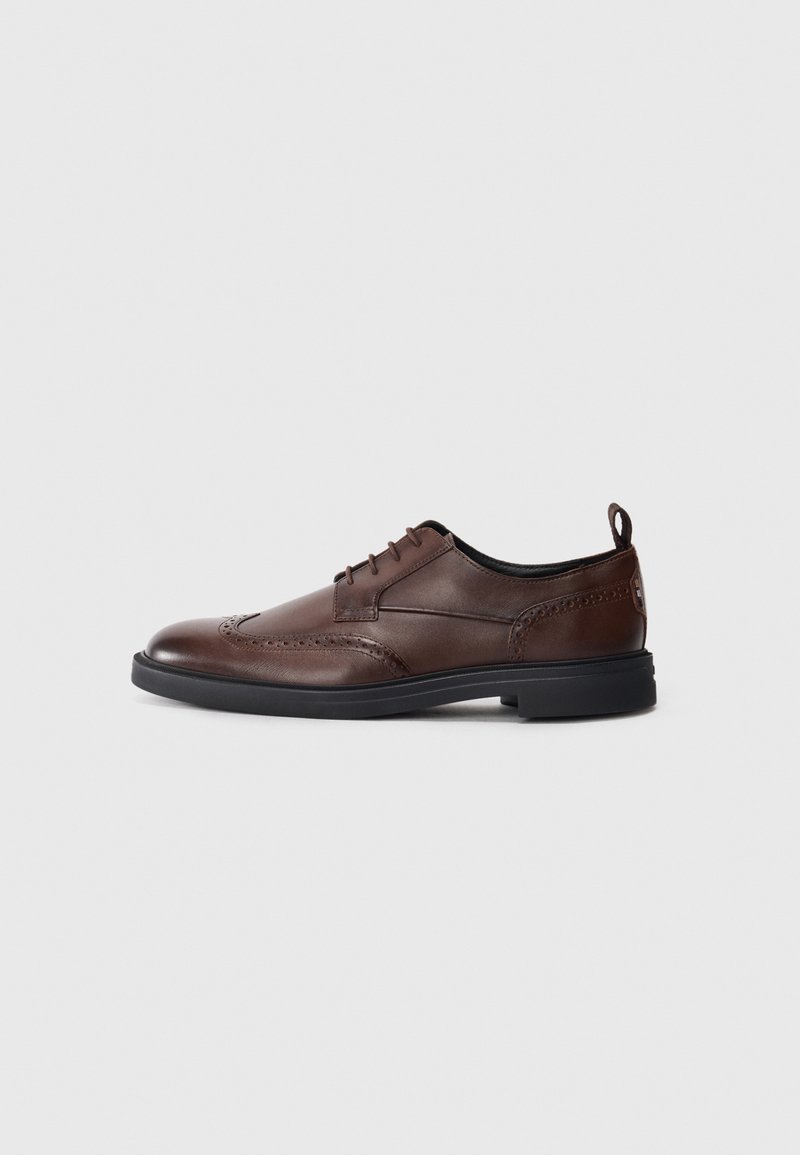Chaussure habillée en cuir marron foncé avec détails brogue, semelle noire, design à lacets et languette au talon, vue du côté extérieur.