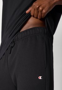 Czarne bawełniane spodnie dresowe z elastycznym pasem i sznurkiem do wiązania. Posiadają boczną kieszeń oraz małe logo na udzie.