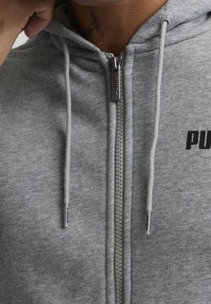 Grå zip-up hoodie av mjuk bomull med huva, dragsnören och en svart logotyp på bröstet. Dragkedja framtill och texturerat tyg.