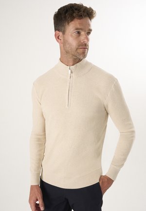 Beige gerippter Strickpullover mit hohem Kragen und Viertelreißverschluss. Figurbetontes Design mit langen Ärmeln und glatter Textur.