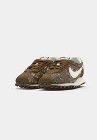 Bruine sneakers met een bovenwerk van textiel met bloemenpatroon, witte Nike swoosh en rubberen loopzool met grip. Compact ontwerp en veterluiting.