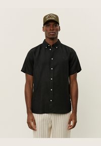 Zwarte korte mouwen button-up shirt van een gestructureerde stof, met een subtiele logo op de borst en witte knopen, gedragen met gestreepte broek.