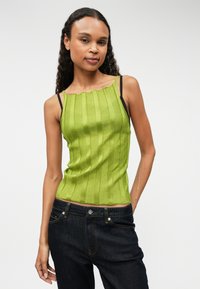 Zielony top na ramiączkach z falbaniastym dekoltem i czarnymi paskami, zestawiony z ciemnoniebieskimi dżinsami. Gładka faktura, dopasowany krój oraz pionowe linie.