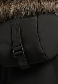 Black padded jacket featuring a brown faux fur collar, with a black strap and buckle detail for secure closure. Smooth fabric texture.