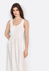 Vestido blanco de algodón con escote redondo, corsé ajustado y falda acampanada. Presenta dos bolsillos frontales y una textura suave.