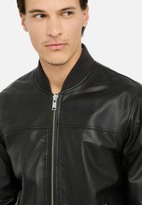 Giubbotto bomber in pelle nera con zip frontale, colletto a coste e texture liscia. Presenta una cucitura orizzontale sul petto.