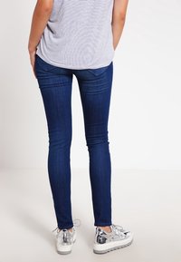 Jeans skinny azul oscuro con una textura suave, con una cintura de altura media y bolsillos traseros, combinados con zapatillas de plataforma plateadas.