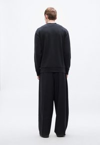 Μαύρο φούτερ και παντελόνι με φαρδιά μπάτζα, με άνετη εφαρμογή, ριμπ μανσέτες και λεία υφή, από πίσω με φόντο λευκό.