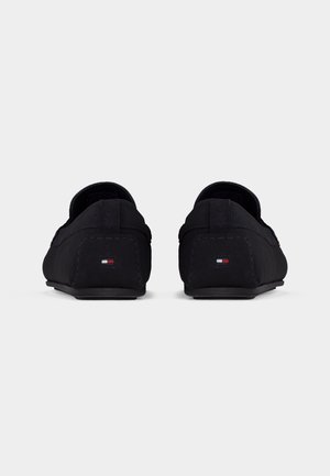 Par sorte slip-on loafers vist bagfra med lille rektangulært logo i rød, hvid og blå på hver hæl.