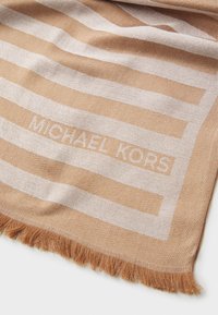 Écharpe beige avec des rayures blanches alternées, présentant un tissage texturé et des bords frangés. Le nom de la marque "MICHAEL KORS" est subtilement intégré.
