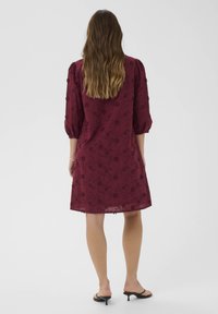 Burgundy klänning med blomsterbroderi, 3/4 pösiga ärmar och avslappnad passform, tillverkad av lättviktigt tyg. Kjolen slutar ovanför knäna.