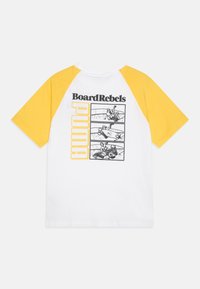 Camiseta de algodón blanca con mangas raglán amarillas. Presenta ilustraciones gráficas en negro y el texto "BoardRebels" y "PUMA" en la parte posterior.