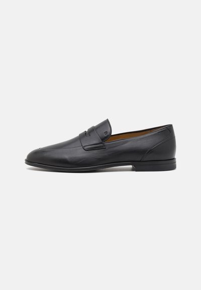 Black leather loafers with a smooth texture, rounded toe, and a small decorative strap across the instep. Flat sole and minimal detailing.