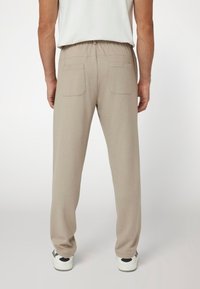 Šviesiai rudos, laisvo kirpimo kelnės su elastinga juosme, dviem užpakalinėm kišenėm ir lygiu paviršiumi. Dėvimos su baltomis sportinėmis bateliais.