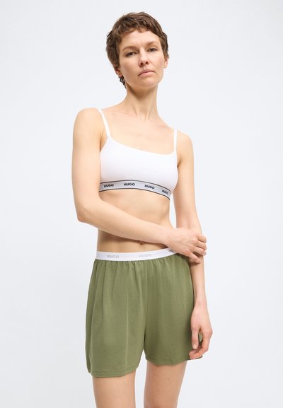 Femme portant un crop top blanc de marque Hugo et un short à taille élastique vert de marque Hugo, debout devant un fond clair uni.