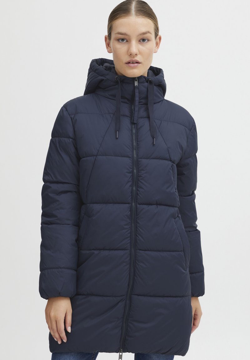Manteau rembourré bleu marine avec capuche, présentant des panneaux matelassés diagonaux, une fermeture éclair à l'avant et des cordons de serrage au niveau du col pour un ajustement près du corps.