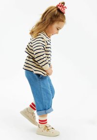 Randig beigefärgad och marinblå långärmad tröja, löst sittande blå denimjeans, beigefärgade skor med röda hjärtan och röd-vita randiga strumpor.