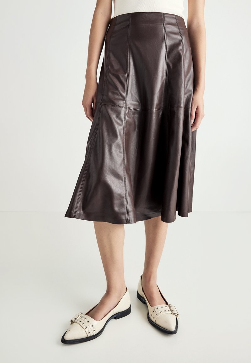 Fustă midi din piele maro cu un design evazat, având cusături vizibile și o textură netedă. Însoțită de pantofi plata de culoare crem.
