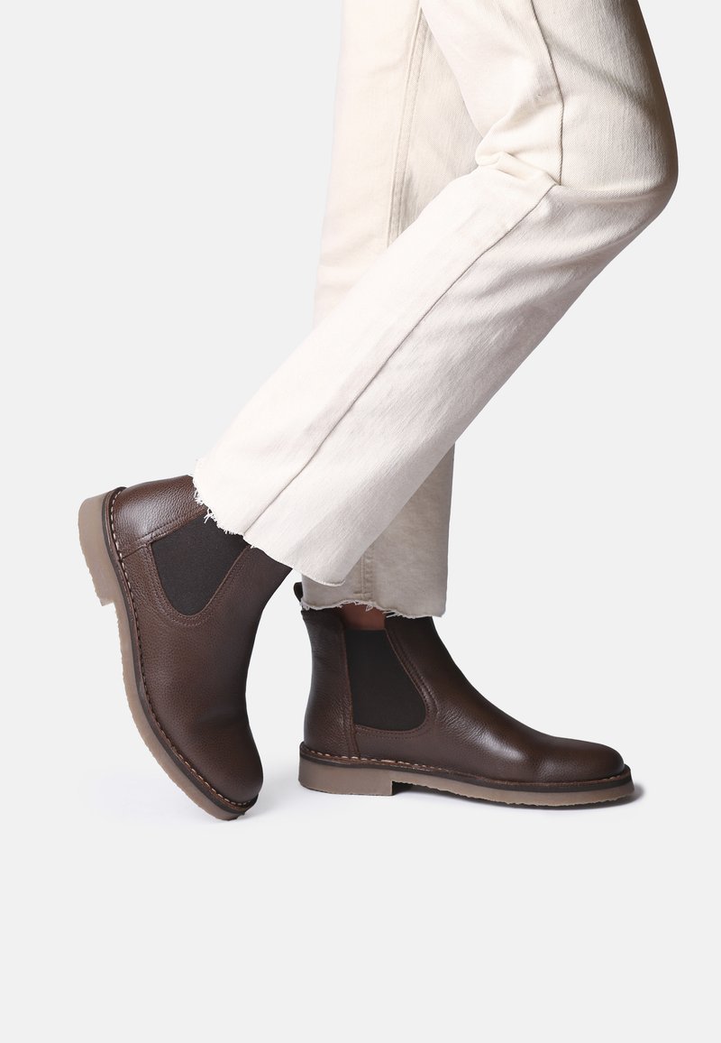 Botas Chelsea de cuero marrón con paneles laterales elásticos, acabado texturizado, suela contrastante y detalle de costura, combinadas con pantalones cortos beige.