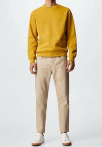 Senfgelbes Crewneck-Sweatshirt, beigen, taillierten Hosen und weißen Sneakers mit braunen Sohlen. Glatter Stoff mit minimalistischem Design.