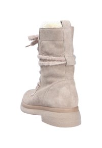 Stivaletto alla caviglia in suede beige con fodera pelosa testurizzata, punta rotonda e lacci morbidi. Presenta una suola in gomma testurizzata bassa per una migliore aderenza.