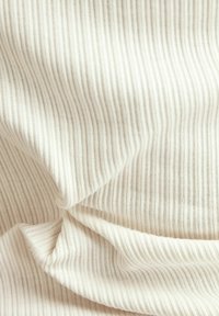 Tela color crema con finas rayas verticales y una textura suave, que muestra pliegues y caídas suaves.