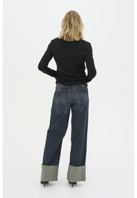 Black long-sleeve top, blue wide-leg jeans with raw hemmed green cuffs, rear view. Fabric appears smooth, jeans have visible pockets.