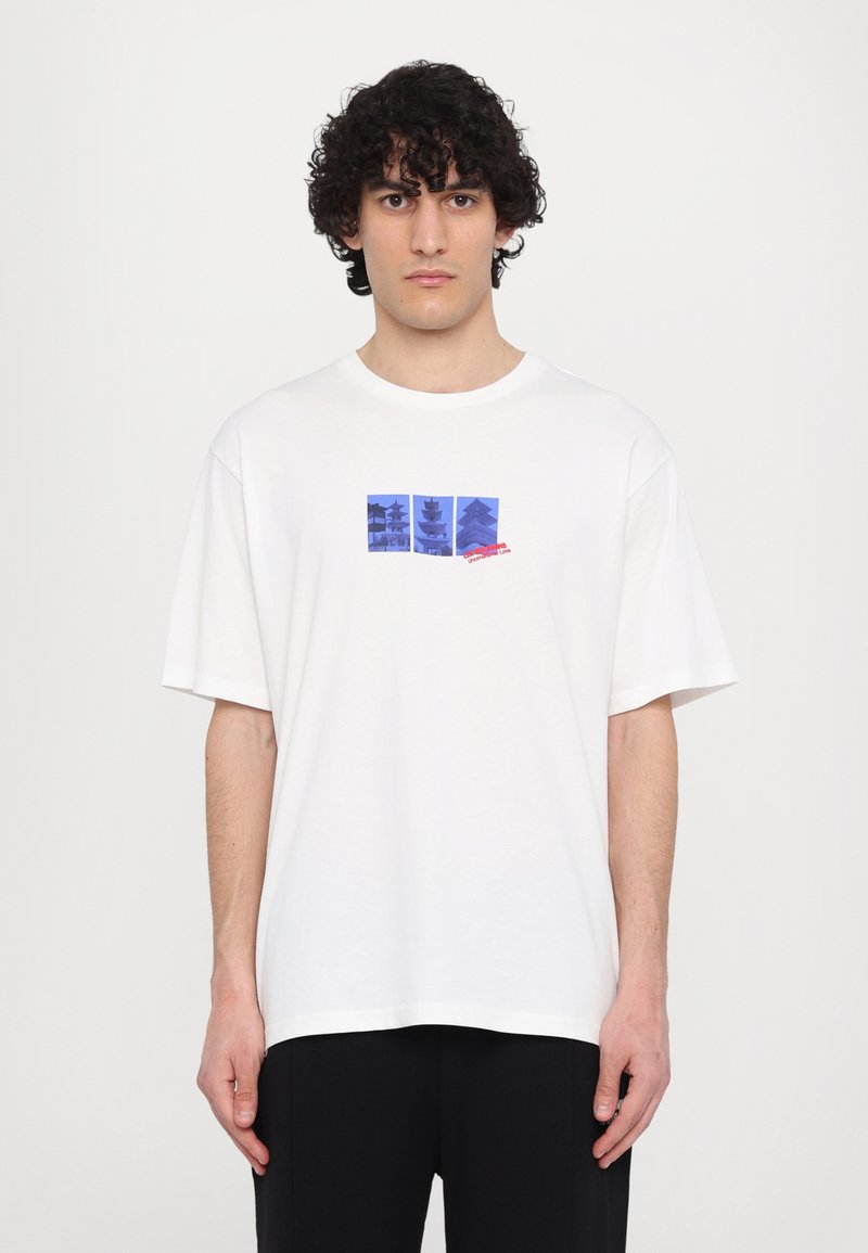 T-shirt en coton blanc avec un imprimé graphique bleu de silhouettes de pagodes et de texte, à manches courtes et coupe décontractée.