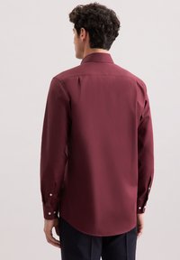 Bordeaux langarmshirt met een klassieke kraag, gladde textuur, knoopmanchetten en een gebogen zoomlijn. Achteraanzicht met schouderplooien.