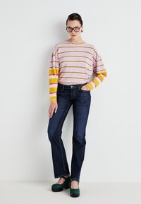 Striped long-sleeve shirt in pink, yellow, and white, paired with dark blue straight-leg jeans and green platform shoes.