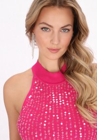 Top halter rosa con paillettes, dal collo alto, caratterizzato da strisce verticali di paillettes lucenti. Capelli lunghi e ondulati aggiungono texture.